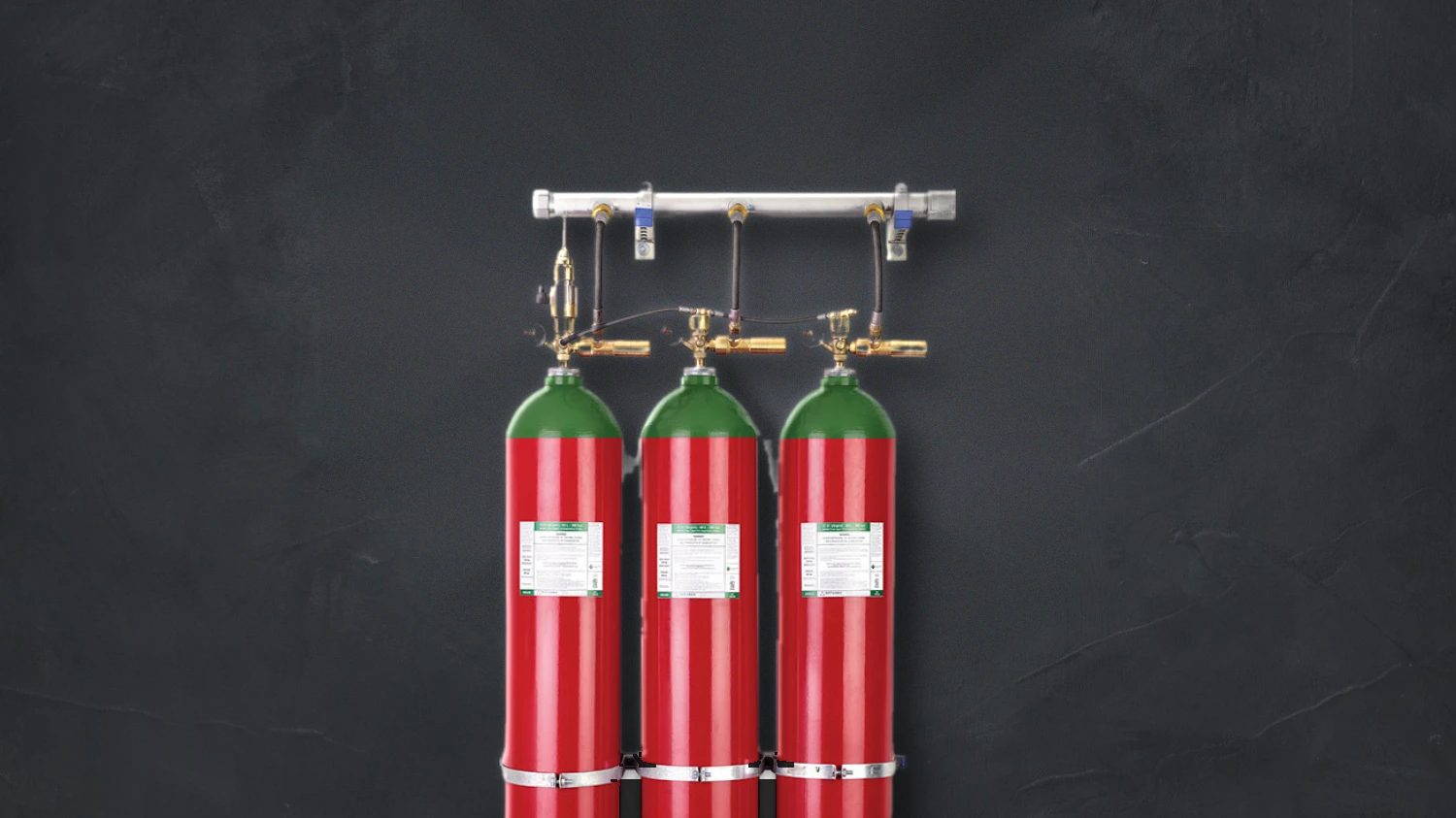 Three red wall-mounted gas suppression cylinders with brass valves and a shared manifold above
